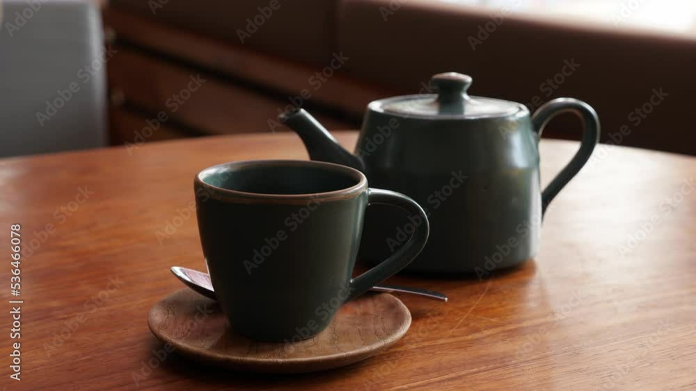Small steam rise fly up from cup with hot Balinese coffee, coffee-pot standing near on wooden table. Still life shot of popular drink served in authentic cafe at Bali Island