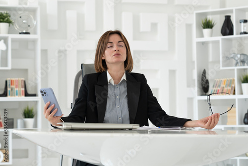 Young attractive business woman sitting at the desk and meditating during the break in the office