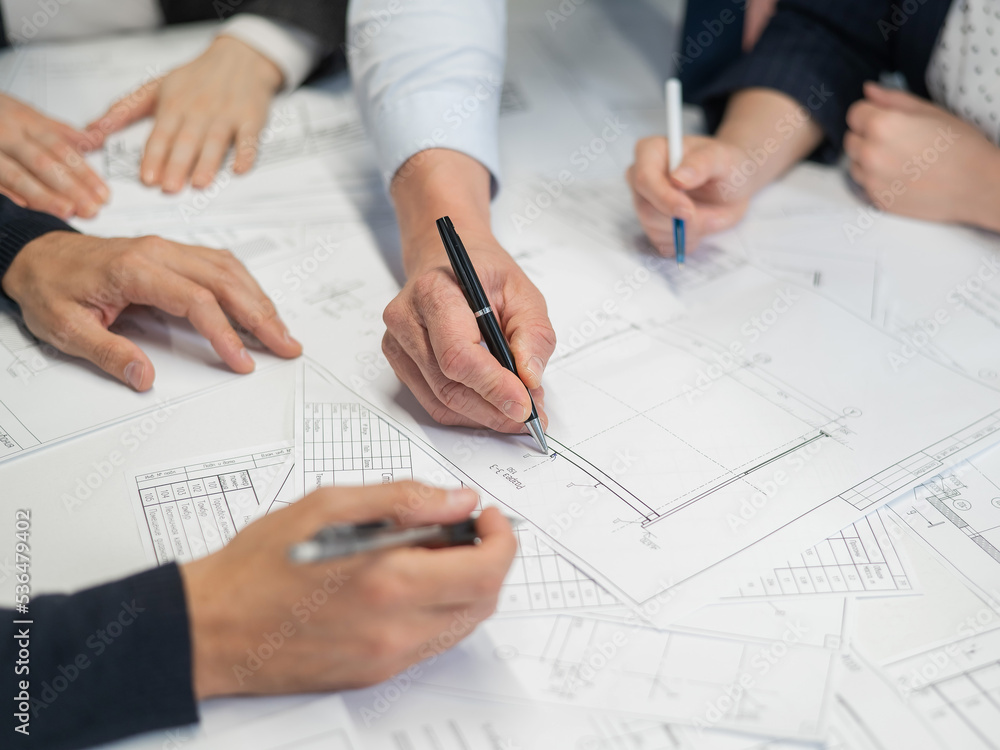 Close-up of the hands of four colleagues with blueprints on the table in the office. Brainstorming of engineers and architects. Close-up of the hands of four colleagues with blueprints on the table in the office. Brainstorming of engineers and architects.