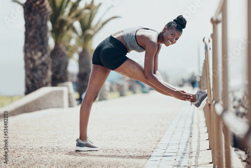 Black woman, stretching and exercise for run, workout and fitness outdoor in street in sunshine. Girl, happy and runner warmup to start training for race, marathon or competition in Cape Town