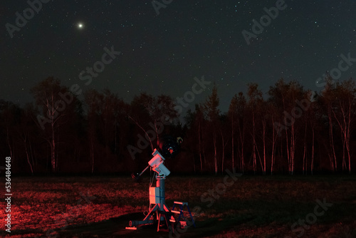 Black telescope on a tripod at the observatory for observation of stars and planets on black sky at night. Science, astronomy concept. Night sky background with a plenty of stars and Jupiter planet