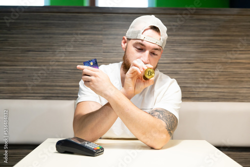 A young man is debating whether to use a credit card or cryptocurrency for payment. Card payment versus bitcoin.