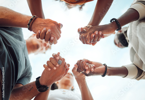 Holding hands, support and friends praying for spiritual growth, community and gratitude together with sky from below. Group of people in partnership for hope, love and human faith in connection photo