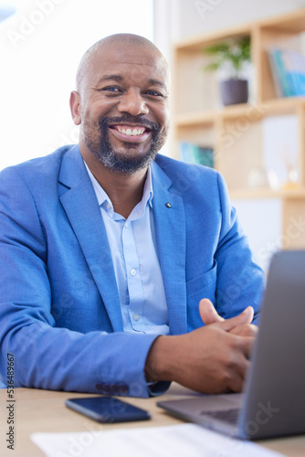 Happy, smile and portrait of an African businessman sitting at his desk and working on a laptop in his office. Happiness, leader and black man leader planning management documents on computer. © Tamline L/peopleimages.com