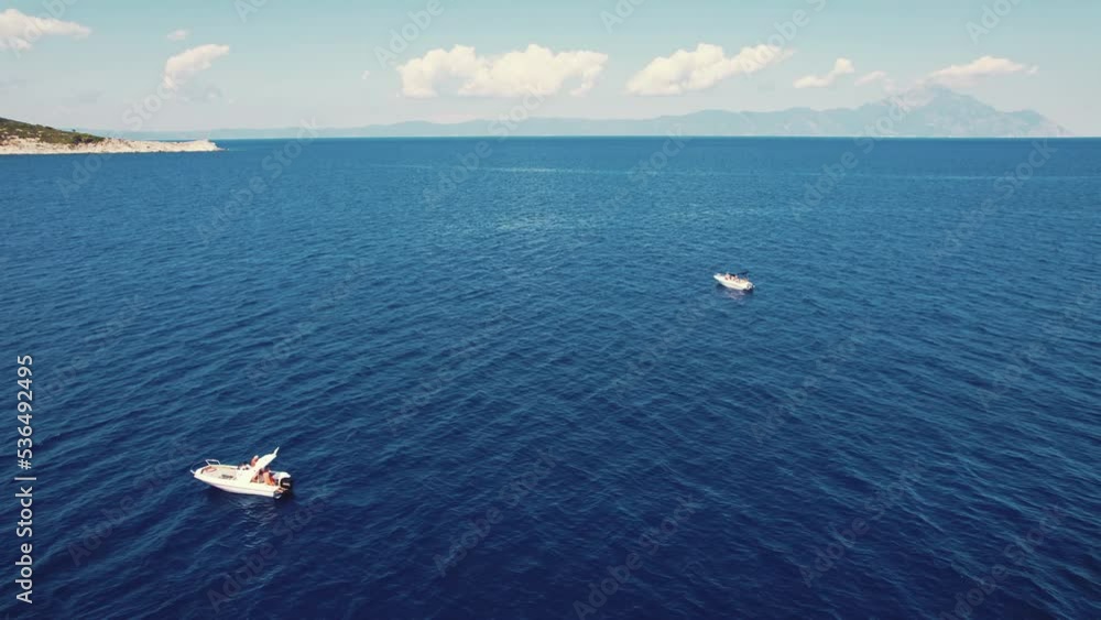 Holidays in Greece. Calm, dark blue seawater with two private white boats with tourists enjoying their time at the seaside and looking at the beautiful Mt. Athos. Drone view. High quality 4k footage Holidays in Greece. Calm, dark blue seawater with two private white boats with tourists enjoying their time at the seaside and looking at the beautiful Mt. Athos. Drone view. High quality 4k footage