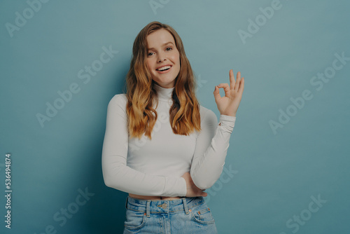 Cheerful excited young woman looking at camera with joyful smile while showing OK sign