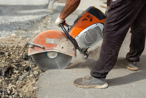 A road builder in uniform cuts off the old asphalt with a hand grinder according to the markings.