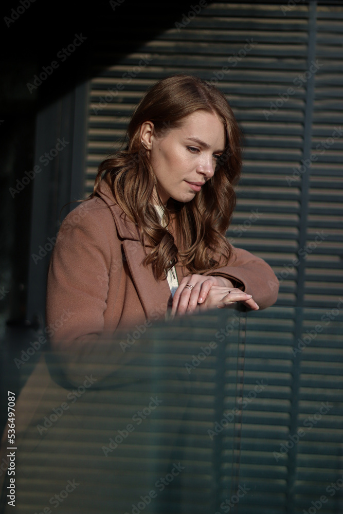 Street photo session of a girl with blond long hair in a beige coat. Photo shoot in the big city. Street photo session of a girl with blond long hair in a beige coat. Photo shoot in the big city.