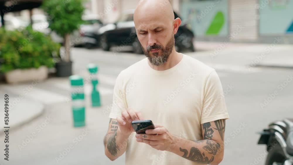 Young bald man using smartphone with serious expression at street Young bald man using smartphone with serious expression at street