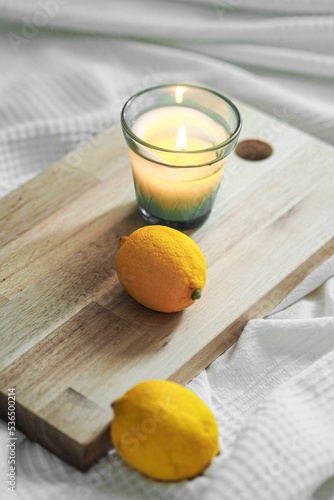 Quadro su tela Vertical closeup shot of a litten candle and oranges on a wooden board, on a whi