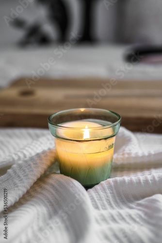 Quadro su tela Vertical closeup shot of a litten candle on a white comforter and a wooden board