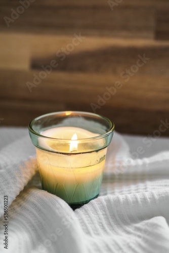 Foto Vertical closeup shot of a litten candle on a white comforter and a wooden board