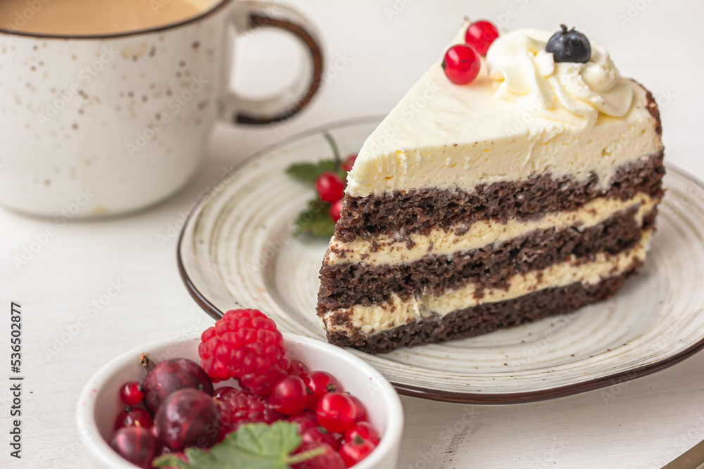 Delicious berry cake. A layered cake with white cream on the plate, a white ceramic cup, a bowl of red berries on white table Delicious berry cake. A layered cake with white cream on the plate, a white ceramic cup, a bowl of red berries on white table