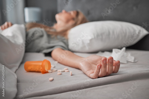 Depression, mental health and overdose with pills and woman in bedroom for anxiety, suicide and death. Sad, medicine and grief with girl lying in bed after taking drugs for pain, trauma and problem