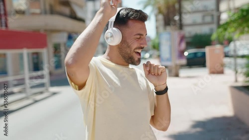 Young hispanic man listening to music and dancing at street