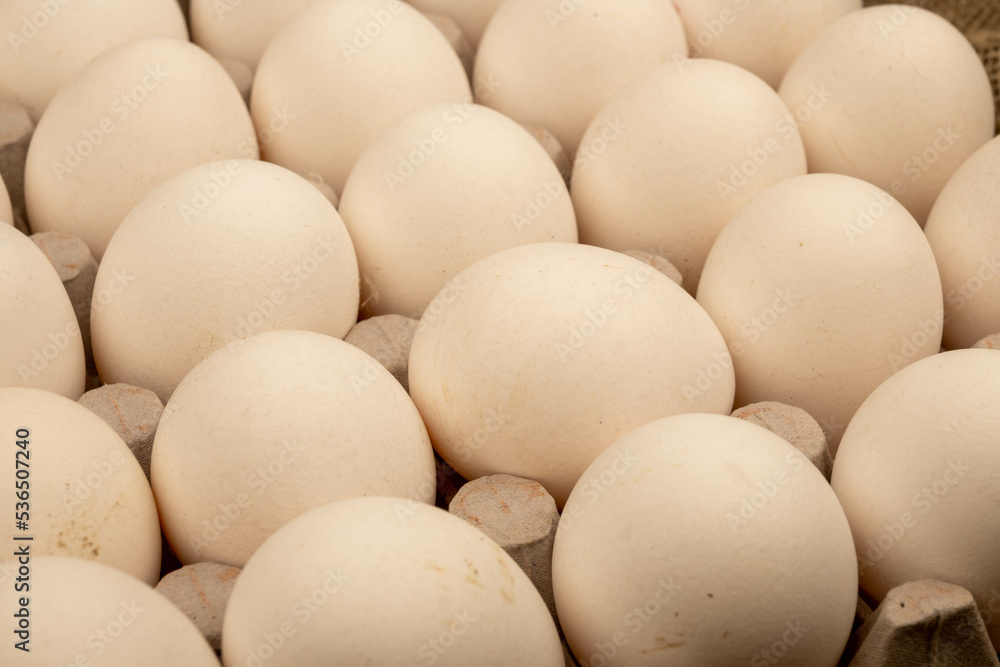 White chicken eggs in a cardboard box on the table. Close-up, selective focus White chicken eggs in a cardboard box on the table. Close-up, selective focus