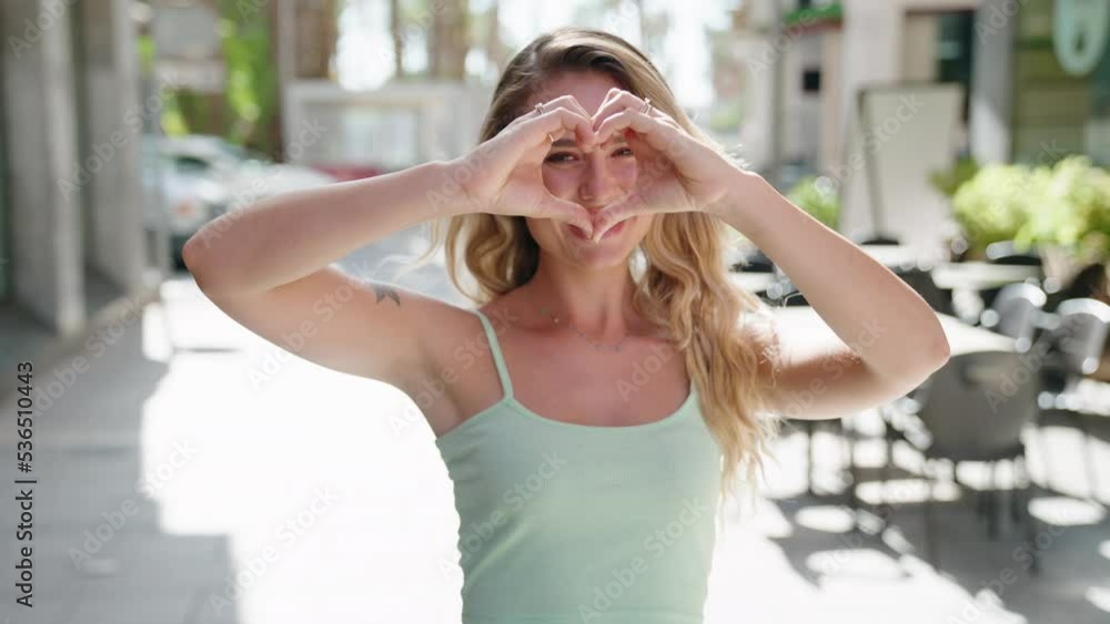Young blonde woman smiling confident doing heart gesture with hands at coffee shop terrace Young blonde woman smiling confident doing heart gesture with hands at coffee shop terrace