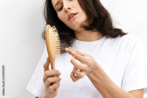 a close horizontal photo of a woman in a white T-shirt on a white background cleaning a comb from fallen hair, looking at the nh with the corners of her lips down