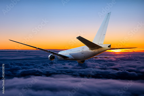 White wide body passenger airliner is flying in the sunset sky