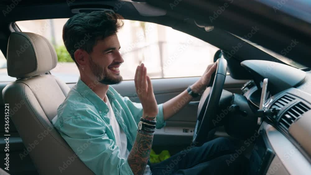 Young hispanic man having video call sitting on car at street Young hispanic man having video call sitting on car at street