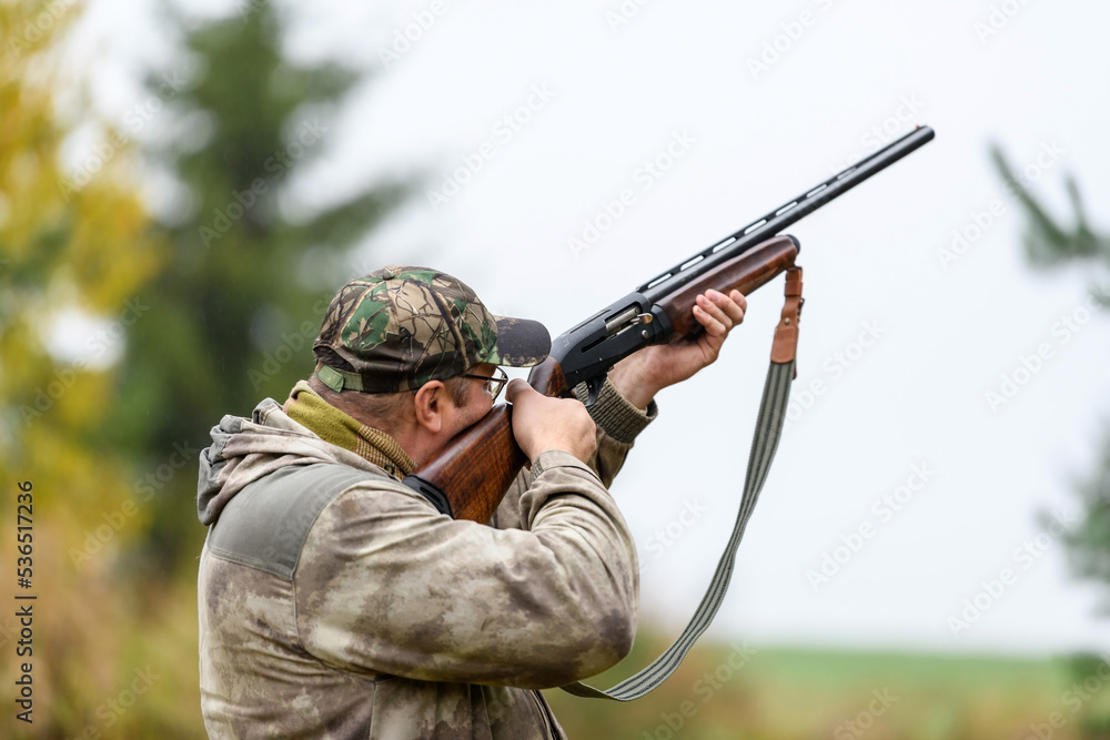 Fototapeta premium The hunter aims at the target - prey from a hunting gun in the forest in light rain. A hunter with a gun in his hands at the opening of the hunting season.Shooting with weapons on the hunt.