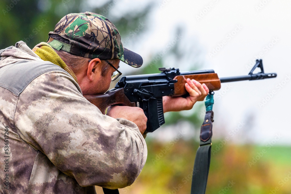 Fototapeta premium A man takes aim and shoots a combat carbine in blurry focus at targets in a shooting range. Back view of a shooting hunter during training.