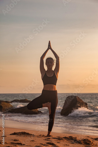 Silhouette young woman on tropical sea coast sandy beach does asana yoga position arms raised outdoors at sunset. Female performs exercises for healthy lifestyle to restore strength, spirit