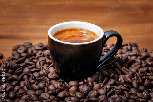 Kawa espresso w czarnej filiżance na drewnianym stole pełnym świeżo palonych ziaren kawy