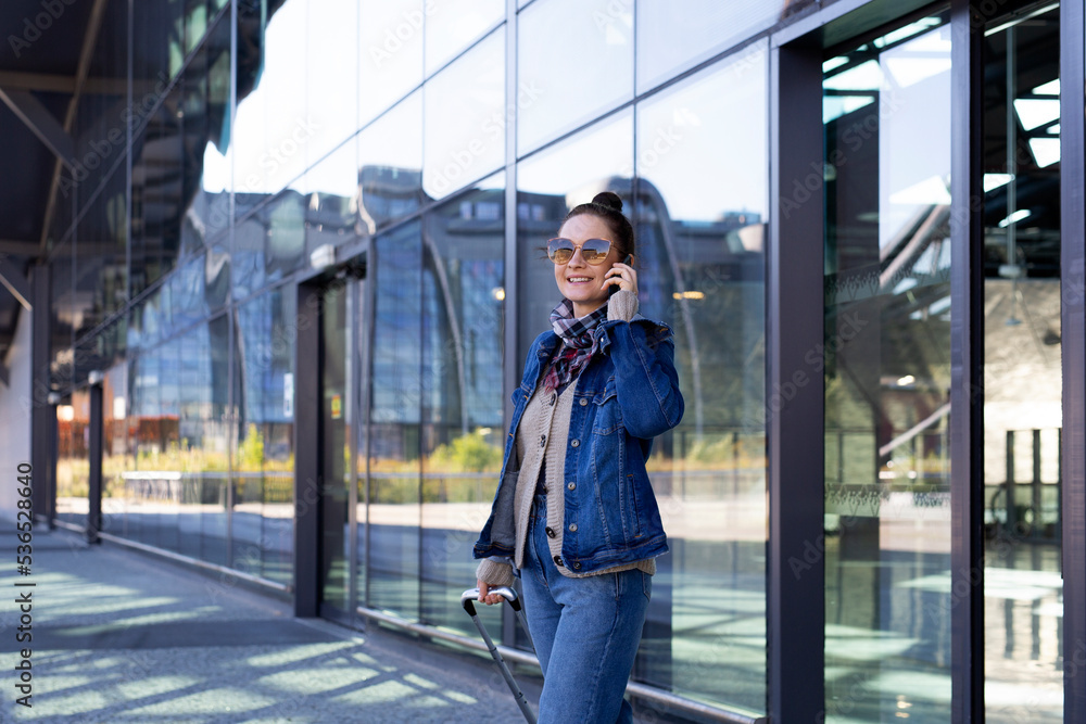 Fototapeta premium Journey. Young woman coming out of the airport talking on the phone.