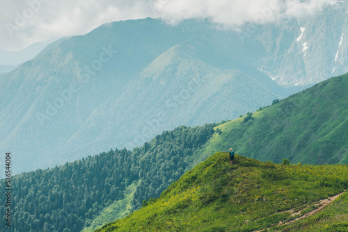 A female traveler on the top of a mountain looks into the distance. Mountain peaks. Krasnaya Polyana, Sochi, Russia. Climbing the mountain.