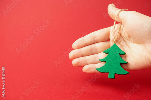 Christmas tree toy in the shape of a Christmas tree hand holding a string on a red background ,the concept of Christmas and Christmas sales
