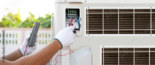Technician air conditioning repairman using measuring equipment checking electrical at circuit breaker on outdoor air compressor after install and check refrigerant system for maintenance.