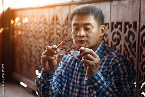 Asian middle aged man holds eyeglasses to check lens. concept   Eyesight problem. Optometry. Glasses with convex or concave lenses. Myopia.Eye disease  