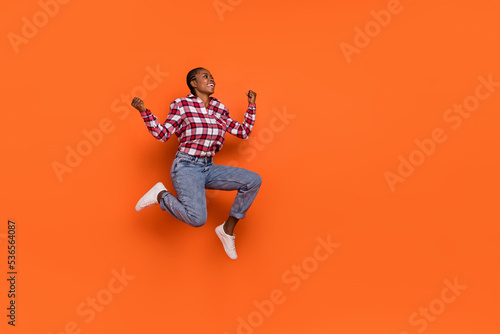Full size portrait of astonished satisfied girl jumping raise fists celebrate isolated on orange color background © deagreez