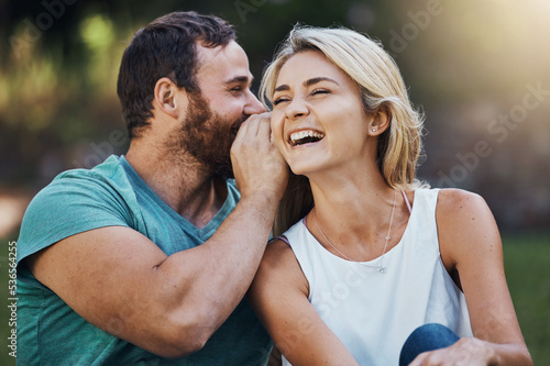 Gossip, secret and funny story with couple on a romantic date in nature in Australia in summer. Man talking in a whisper into the ear of a young laughing woman while happy in a garden together photo