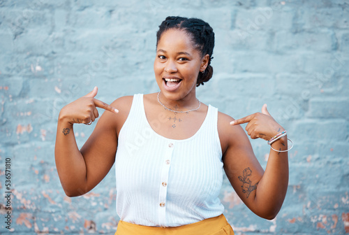 Black woman, pointing and happy feeling proud and self assured choosing herself against city building wall, mockup space or outside in Nigeria. Portrait of African model with a fun or playful gesture photo