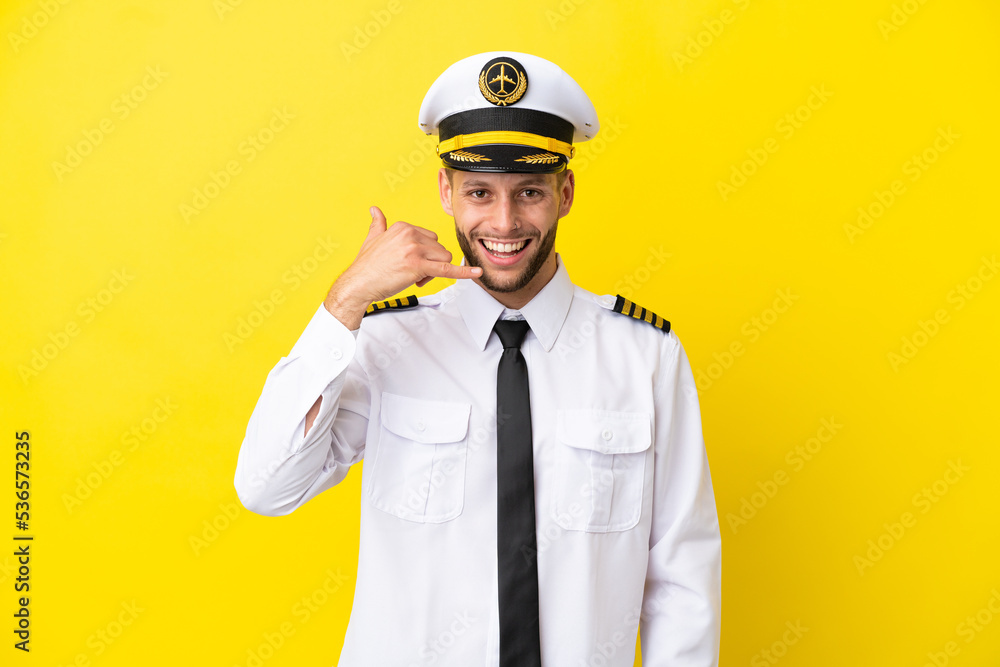 Airplane caucasian pilot isolated on yellow background making phone gesture. Call me back sign Airplane caucasian pilot isolated on yellow background making phone gesture. Call me back sign