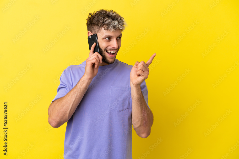 Young caucasian man using mobile phone isolated on yellow background intending to realizes the solution while lifting a finger up Young caucasian man using mobile phone isolated on yellow background intending to realizes the solution while lifting a finger up