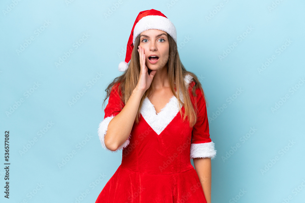 Young caucasian woman dressed as mama noel isolated on blue background with surprise and shocked facial expression Young caucasian woman dressed as mama noel isolated on blue background with surprise and shocked facial expression