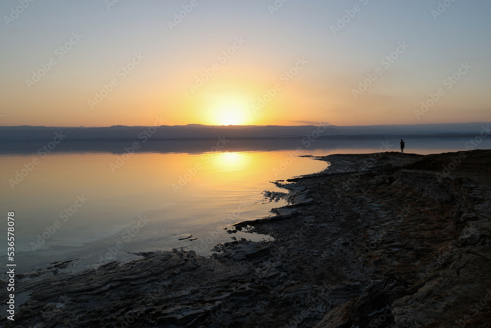 silhouette of man walking on dead sea coastline at sunset