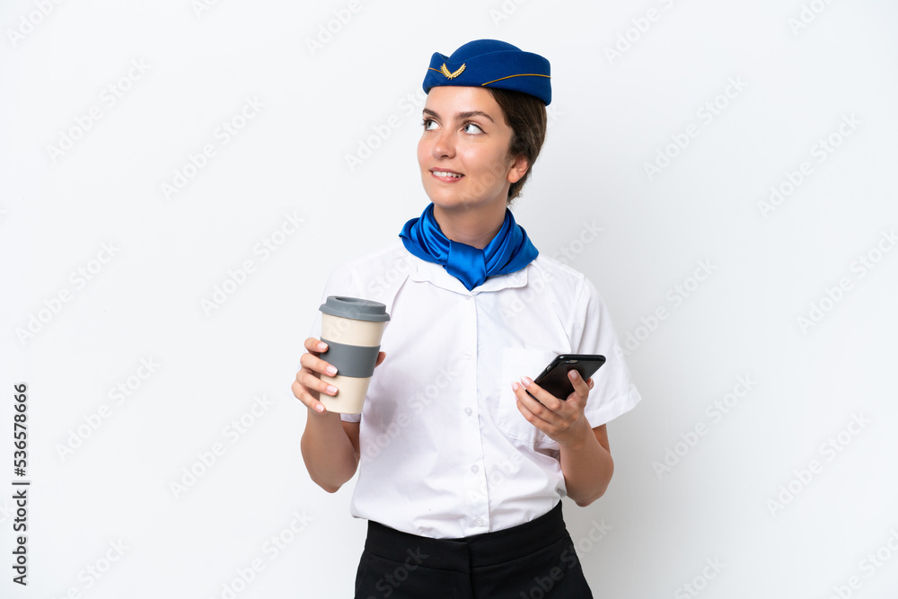 Airplane stewardess caucasian woman isolated on white background holding coffee to take away and a mobile while thinking something Airplane stewardess caucasian woman isolated on white background holding coffee to take away and a mobile while thinking something