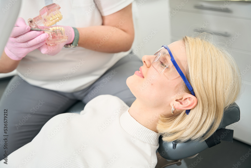 Female patient in goggles looks at the model of the jaw