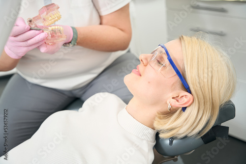 Female patient in goggles looks at the model of the jaw