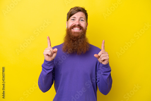 Redhead man with beard isolated on yellow background pointing up a great idea