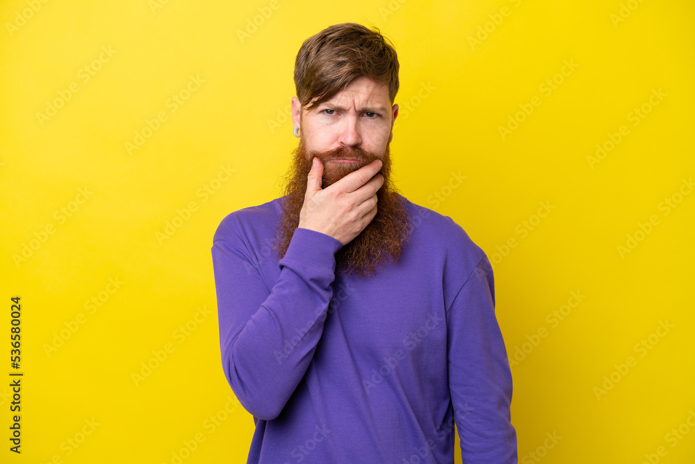 Redhead man with beard isolated on yellow background having doubts