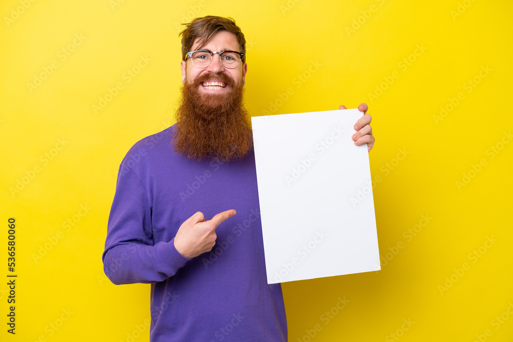 Redhead man with beard isolated on yellow background holding an empty placard with happy expression and pointing it Redhead man with beard isolated on yellow background holding an empty placard with happy expression and pointing it