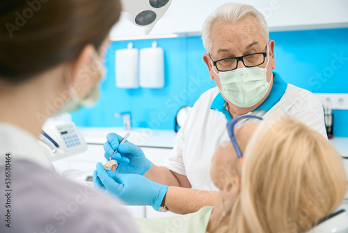 Caucasian orthodontist in protective mask with artificial jaw talking with woman