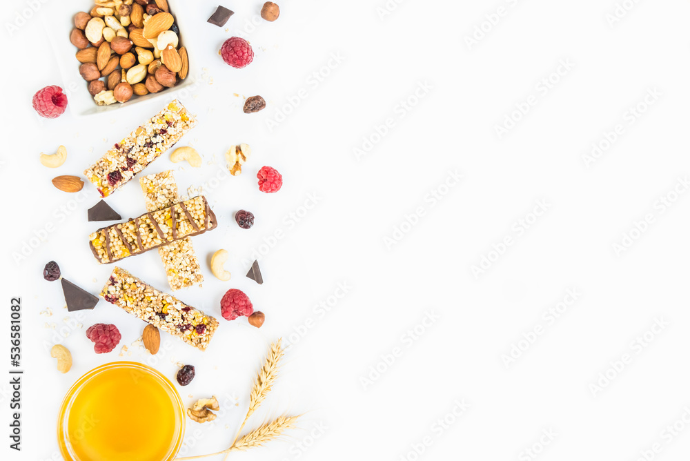 Top view of various homemade granola bars with nuts, seeds, dark chocolate, honey and berries over a white background. Copy space.