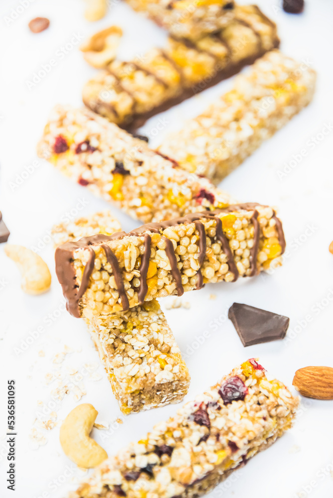 Close view of various homemade granola bars with nuts, seeds, dark chocolate, honey and berries over a white background.