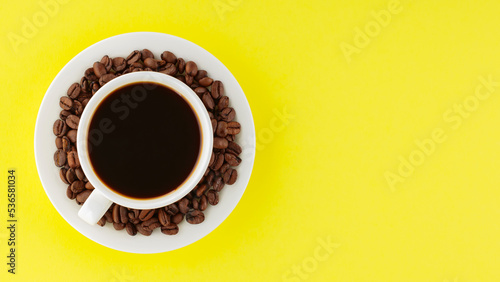 Coffee cup and roasted coffee beans on a saucer. Cup of black coffee on a yellow background. Top view. Copy space © Lazartivan